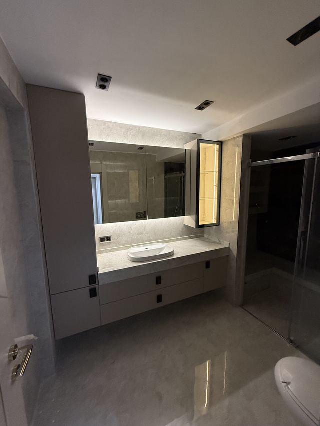 Açık renk lavabo dolabı, boy dolabı ve ışıklı aynalı dolap bulunan banyo